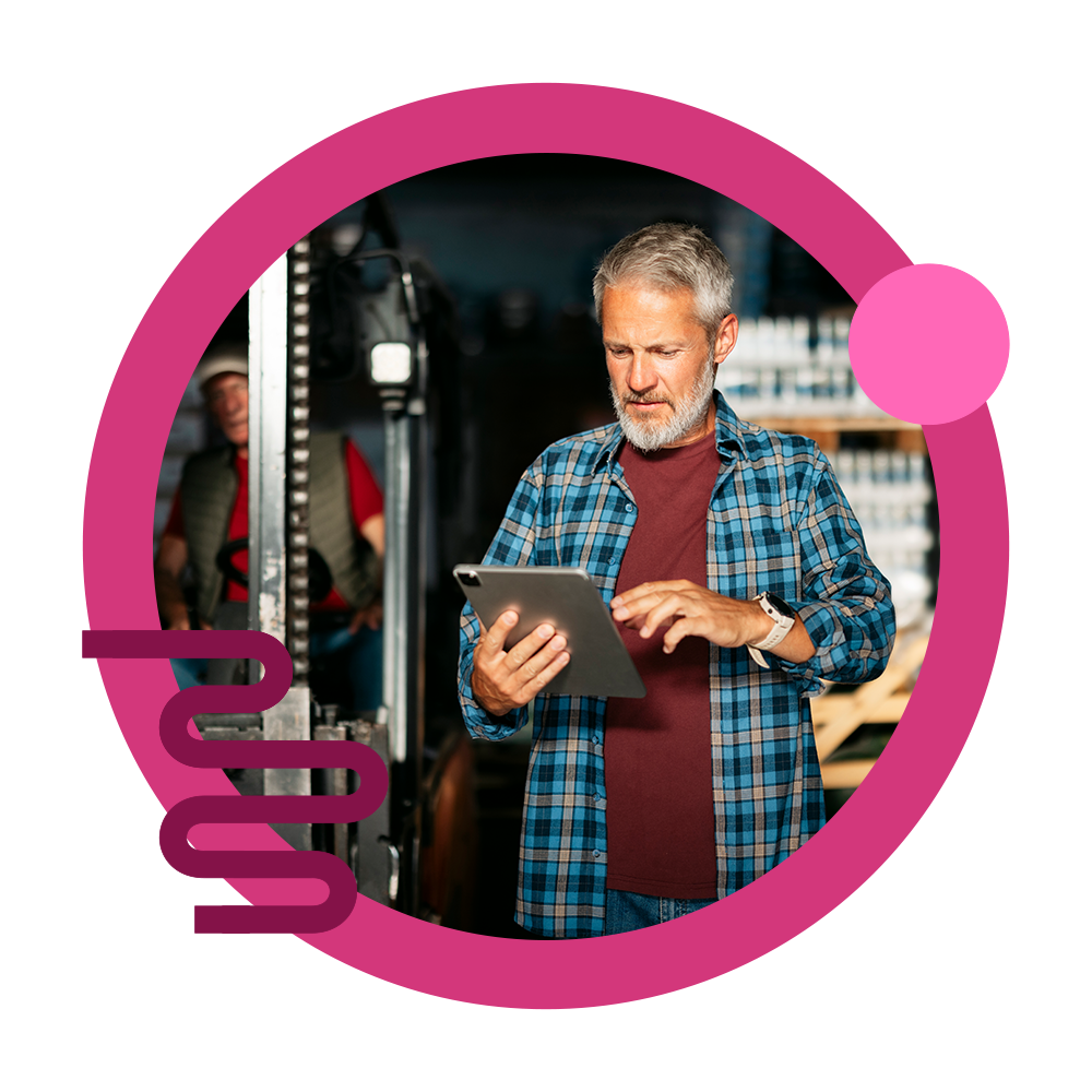 An elderly gentleman on a device in a warehouse.